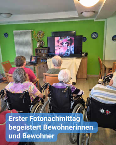 Senioren und Senioren sitzen gemeinsam im Gemeinschaftsraum und schauen sich am Fernseher eine Diashow von Fotos an. Bildbeschriftung: Erster Fotonachmittag begeistert Bewohnerinnen und Bewohner
