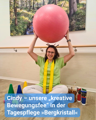 Ergotherapeutin sitzt auf dem Fußboden, umgeben von Pinsel und Farbe für die Kreativität sowie kegeln und Handeln für die sportliche Aktivität. Sie hält lächelnd einen Ball in die Luft. Bildbeschriftung: Cindy – unsere „kreative Bewegungsfee“ in der Tagespflege »Bergkristall«