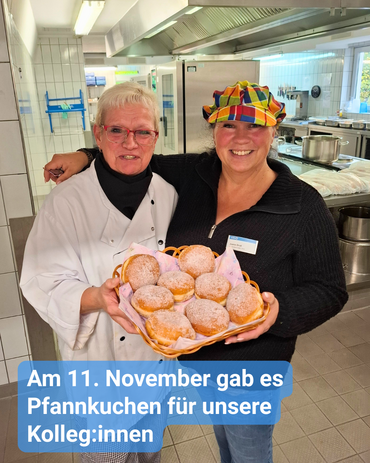 Eine Kollegin überreicht Pfannkuchen an das Team der Küche. Bildbeschriftung: Am 11. November gab es Pfannkuchen für unsere Kolleg:innen