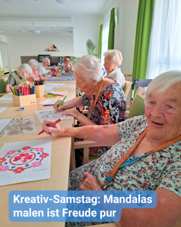 Eine fröhliche Gruppe ist Seniorinnen und Senioren, die gemeinsam an einer großen Tafel sitzen und Mandalas ausmalen. Fröhliche und ausgelassene Stimmung. Bildunterschrift: „Kreativ-Samstag: Mandala malen, ist Freude pur.”