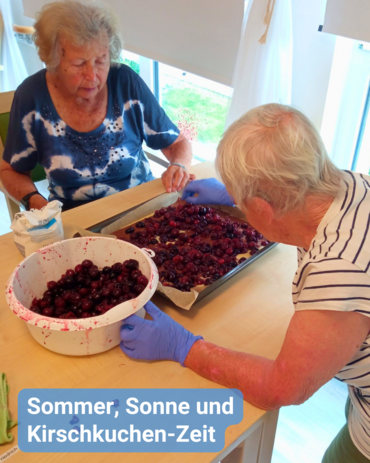 Zwei Frauen mit Handschuhen belegen einen Kuchen mit Kirschen auf einem Blech. Text: 'Sommer, Sonne und Kirschkuchen-Zeit'.