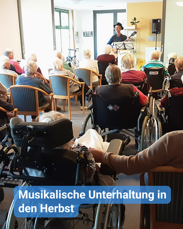 Musiker mit Hut und Gitarre spielt und singt vor einem älteren Publikum. Bildbeschriftung: “Musikalische Unterhaltung in den Herbst”
