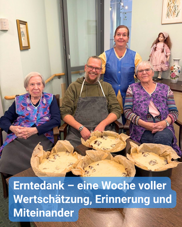 Zwei Seniorinnen und zwei Betreuungskräfte – alle tragen Schürzen – sitzen vor einem Tisch mit vier Kuchenformen. Stolz präsentieren sie den selbstgemachten Pflaumenkuchen. Bildbeschriftung: „Erntedank – eine Woche voller Wertschätzung, Erinnerung und Miteinander“