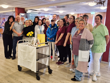 Das Team steht beieinander und lächelt in die Kamera. Vor ihnen ein Wagen mit Blumen und Dekoration